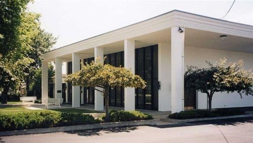 Modern white office building with tall columns and landscaped trees outside