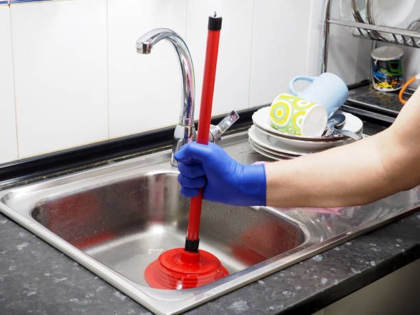 A person is using a plunger to clean a kitchen sink.