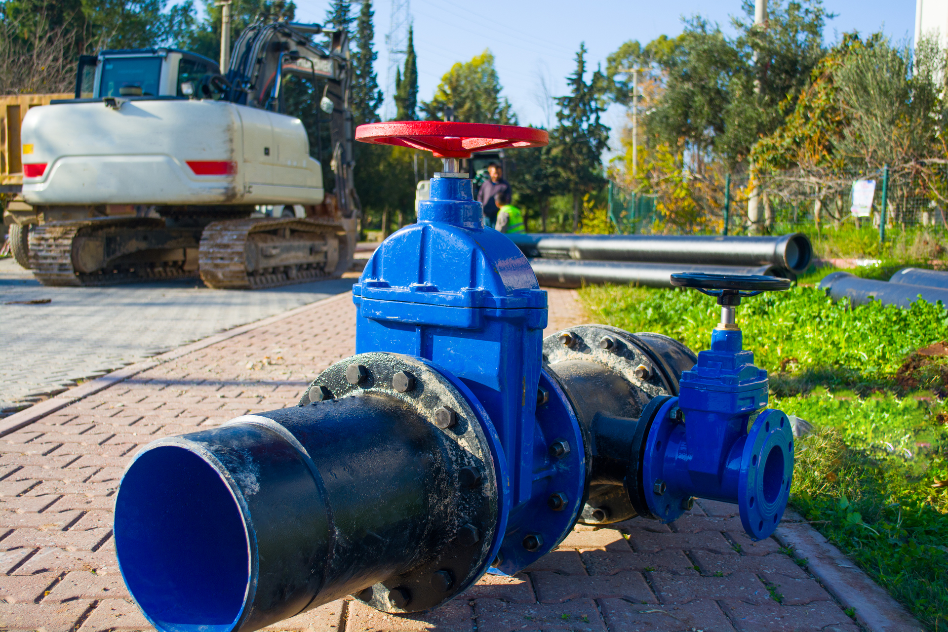A blue pipe with a red handle is sitting on a sidewalk next to a bulldozer.