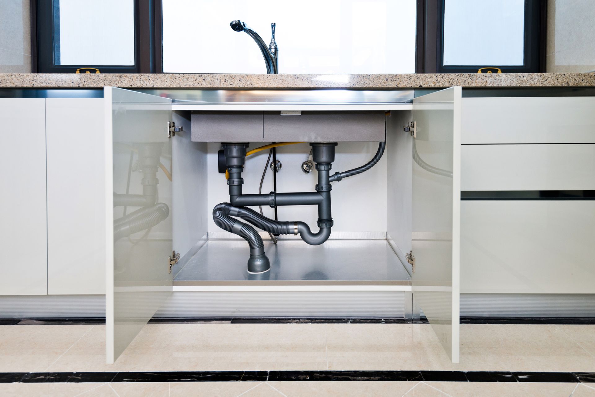 A kitchen sink is under a cabinet with the doors open