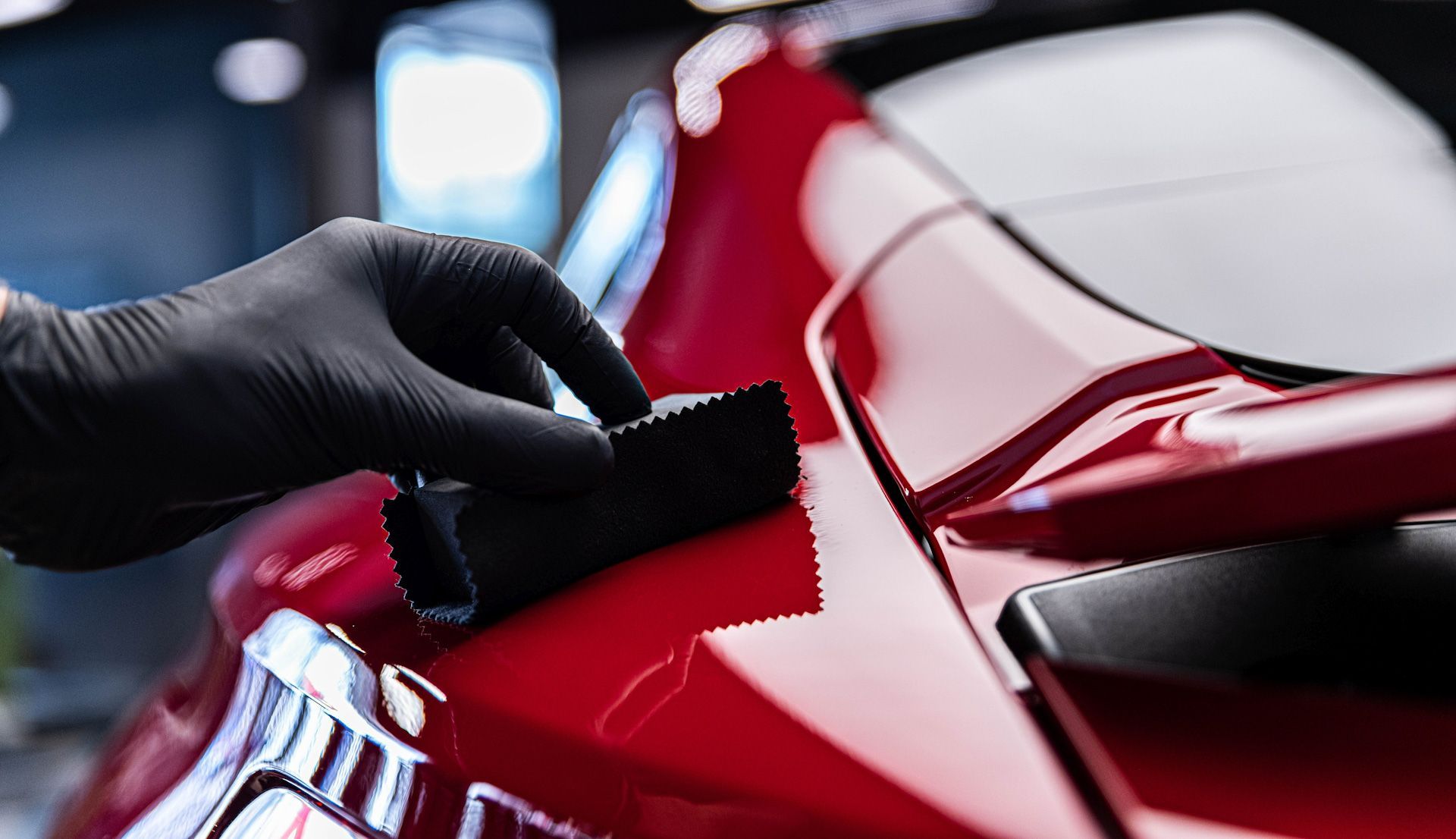 A person wearing black gloves is polishing a red car.