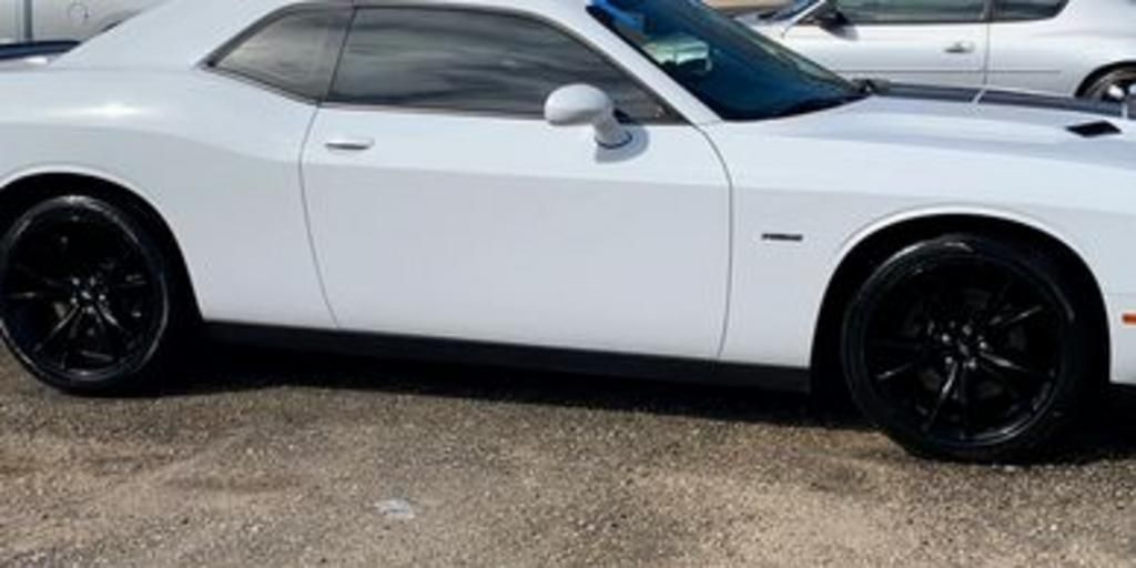 A white dodge challenger is parked in a parking lot.