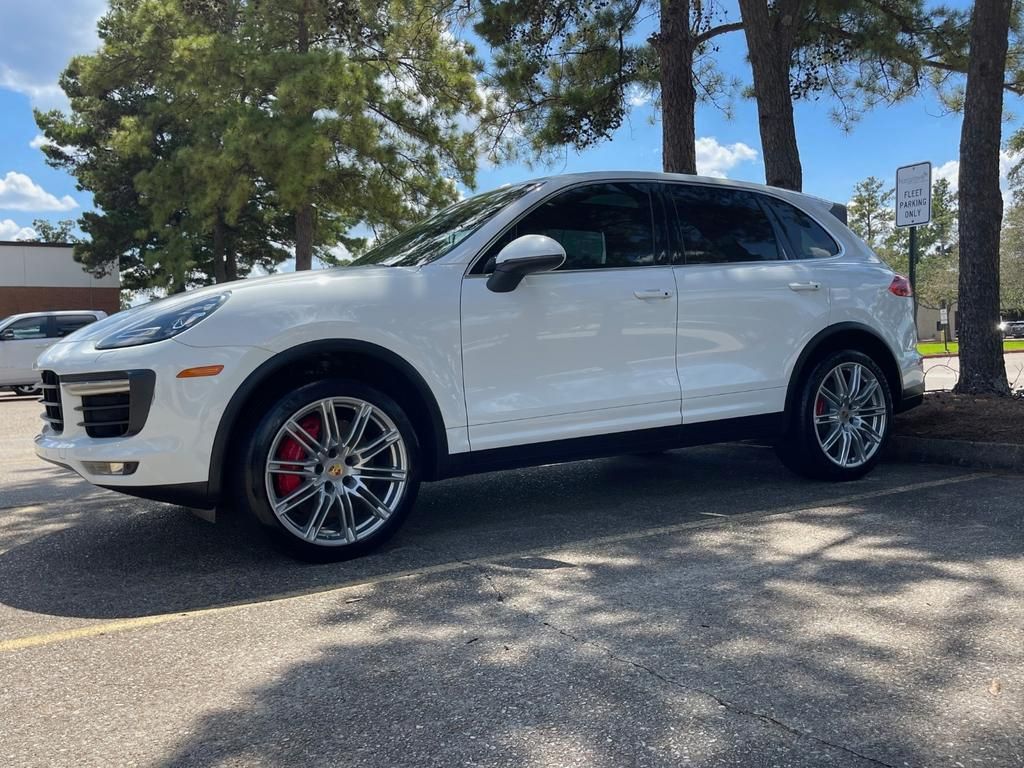 A white porsche cayenne is parked in a parking lot.