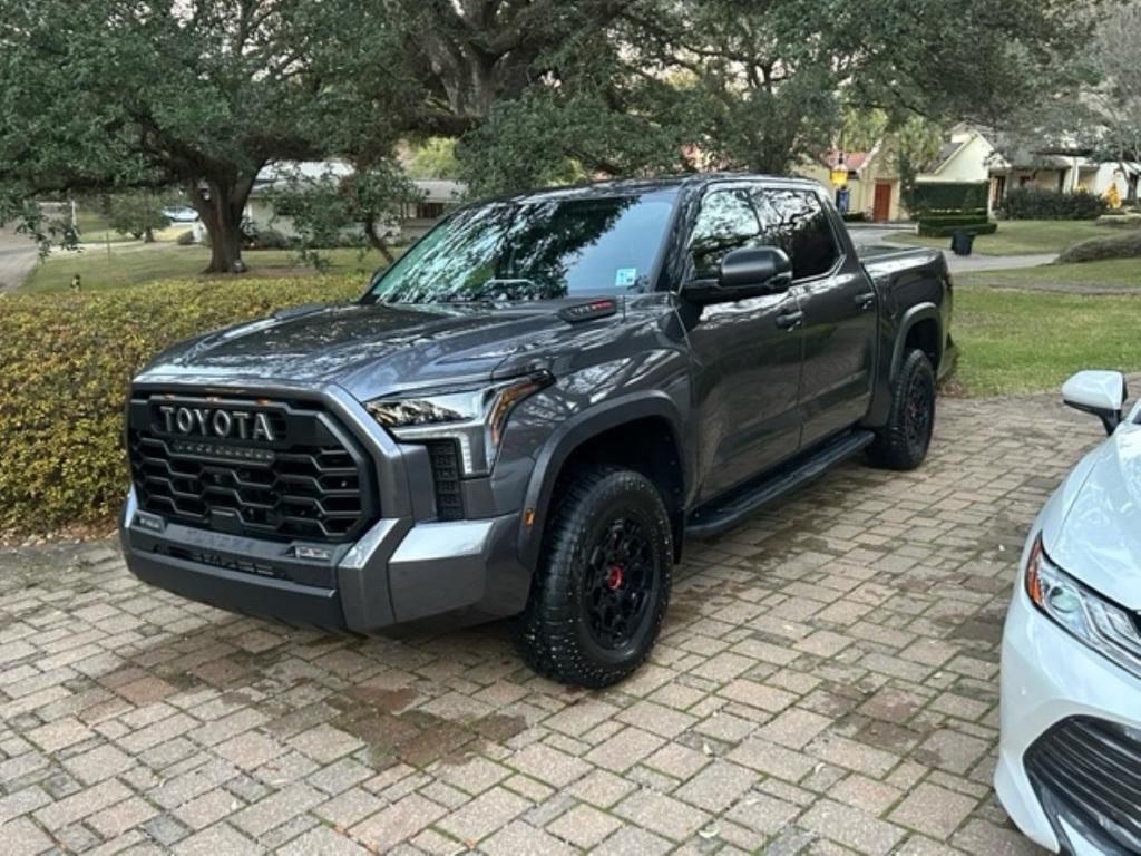 A toyota tundra is parked on a brick driveway next to a white car.