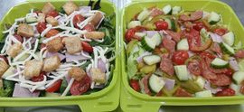 Two green trays of salad with lettuce, tomatoes, cucumbers, croutons, and shredded cheese