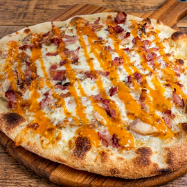 Close-up of a cheesy pizza with bacon and orange sauce on a wooden board