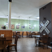 Cozy café interior with wooden tables, mint-green walls, hanging lights, and a “Coming Soon” sign on a pillar