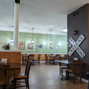 Cozy café interior with wooden tables, mint-green walls, hanging lights, and a “Coming Soon” sign on a pillar