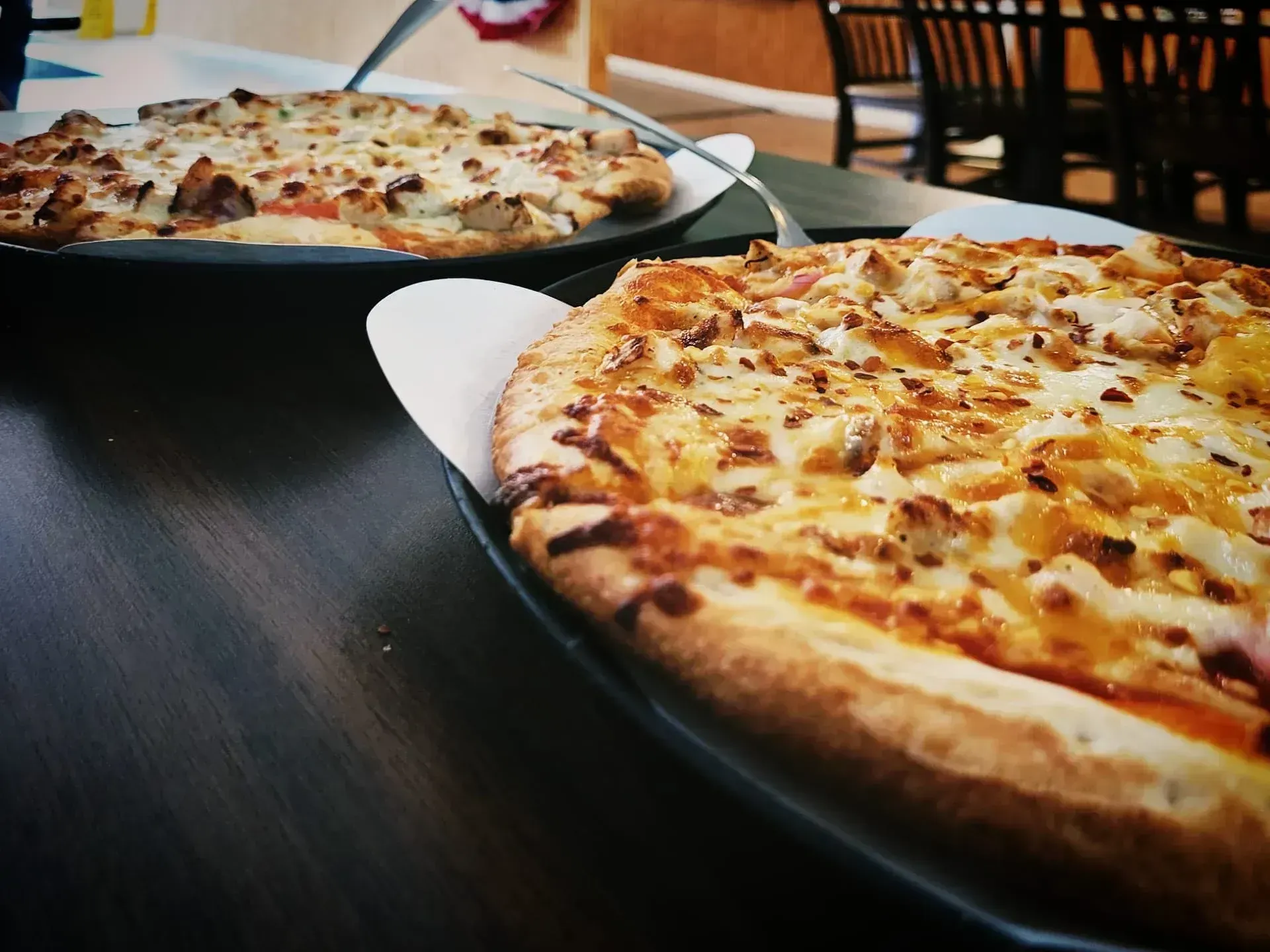 Two cheese pizzas on black plates on a dark table in a restaurant or cafe