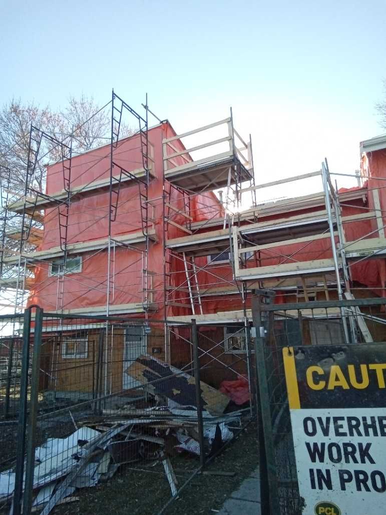 Building under construction, wrapped in red, with scaffolding. Warning sign in foreground.