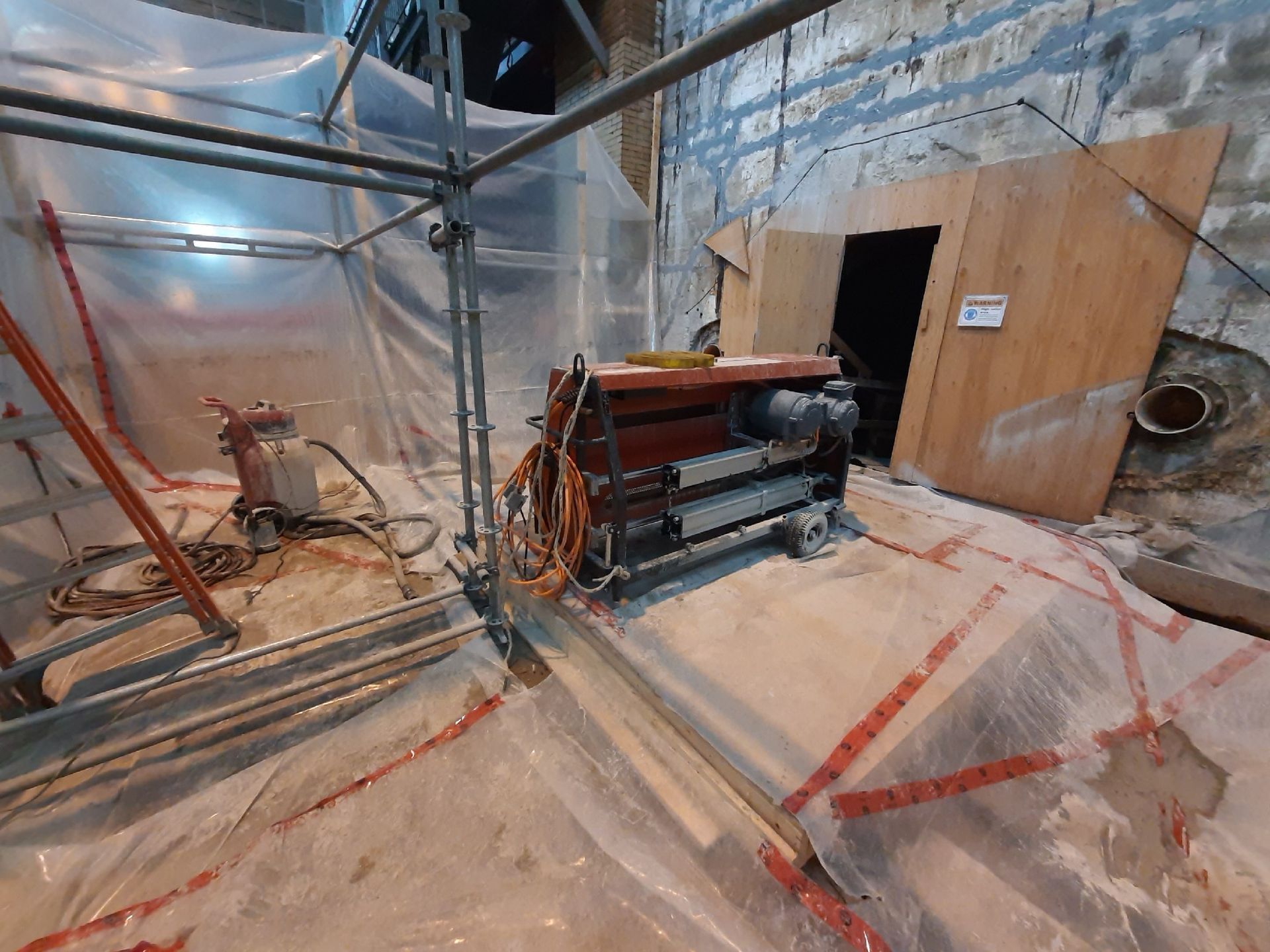 Construction site with scaffolding and machinery. Protective plastic covers the floor and walls.