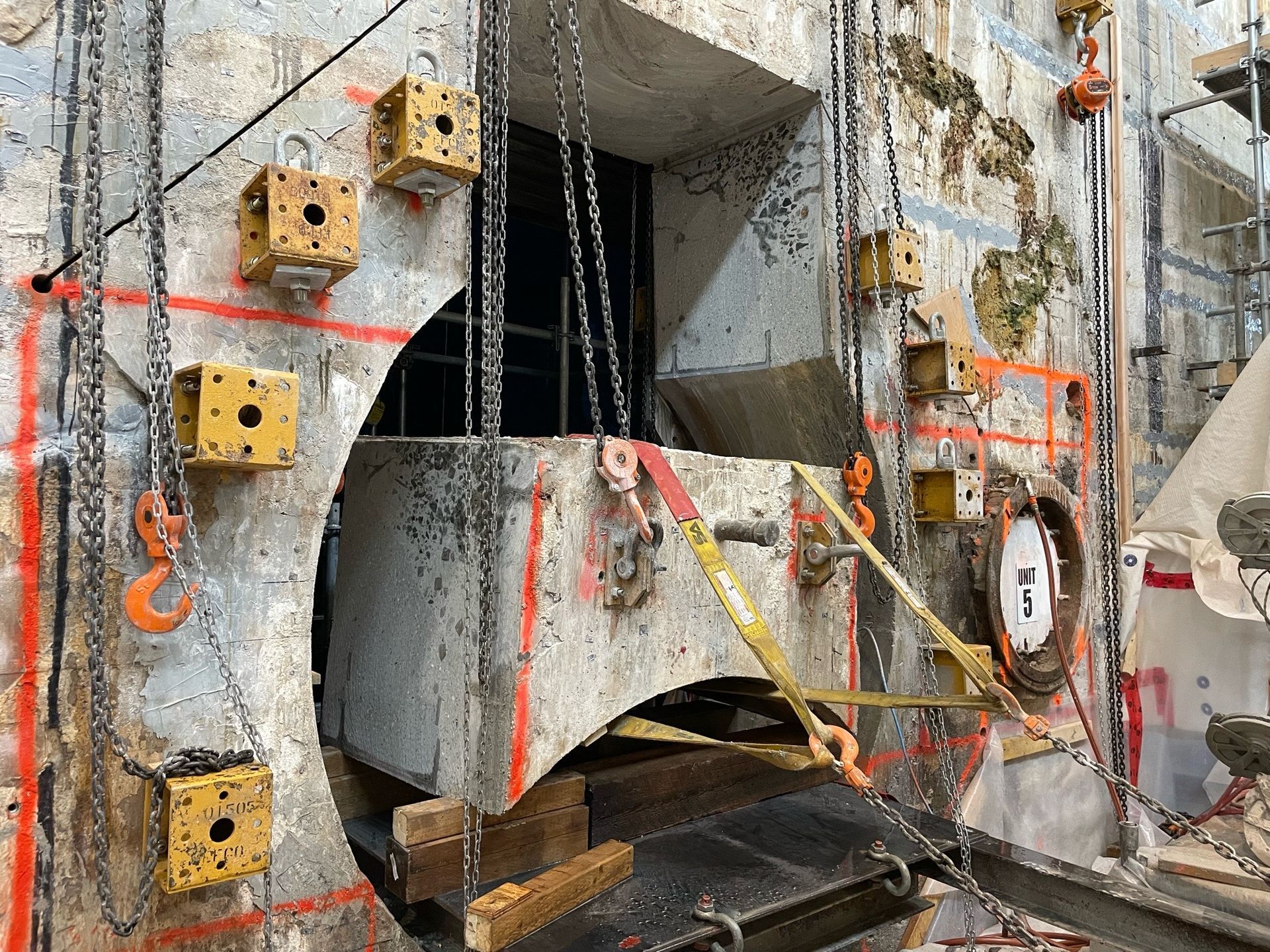 Construction site with concrete wall, a round opening, chains, and yellow lifting blocks.