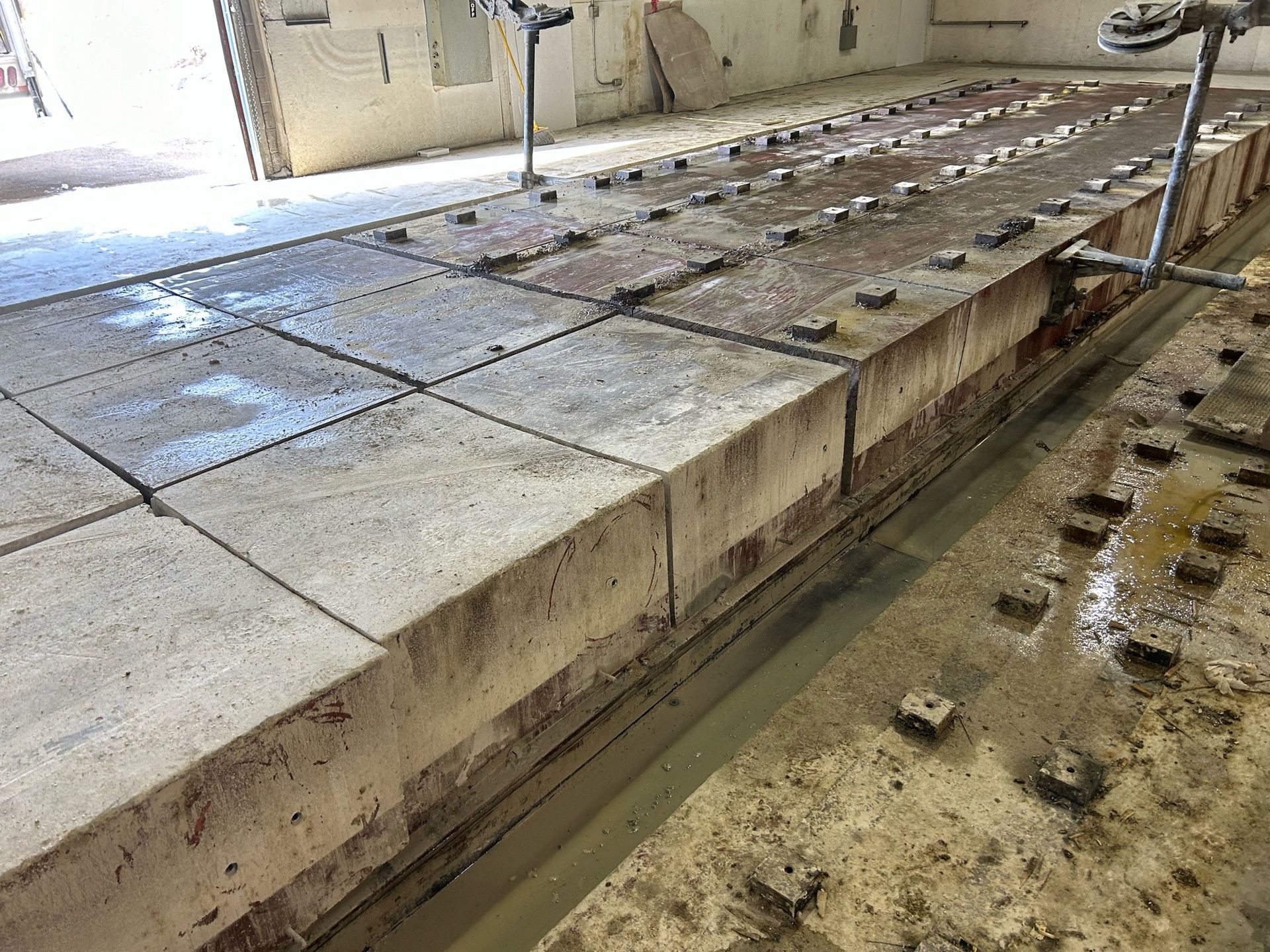 Concrete blocks stacked in a row, with metal hardware and water visible. Industrial setting.