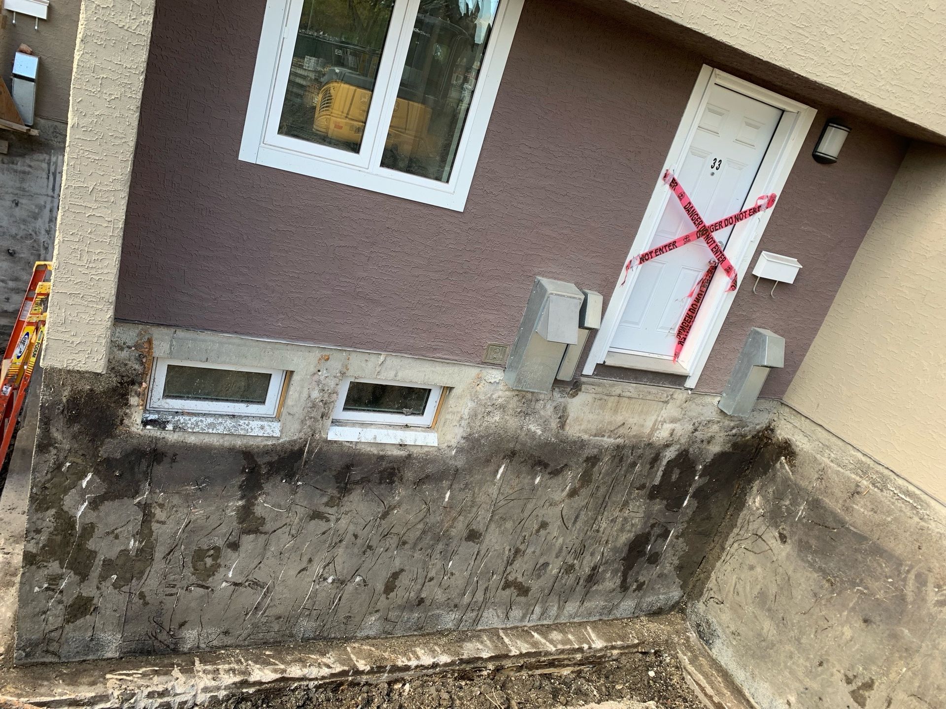 Exterior of a building with a white door sealed with red tape, windows, and exposed concrete foundation.