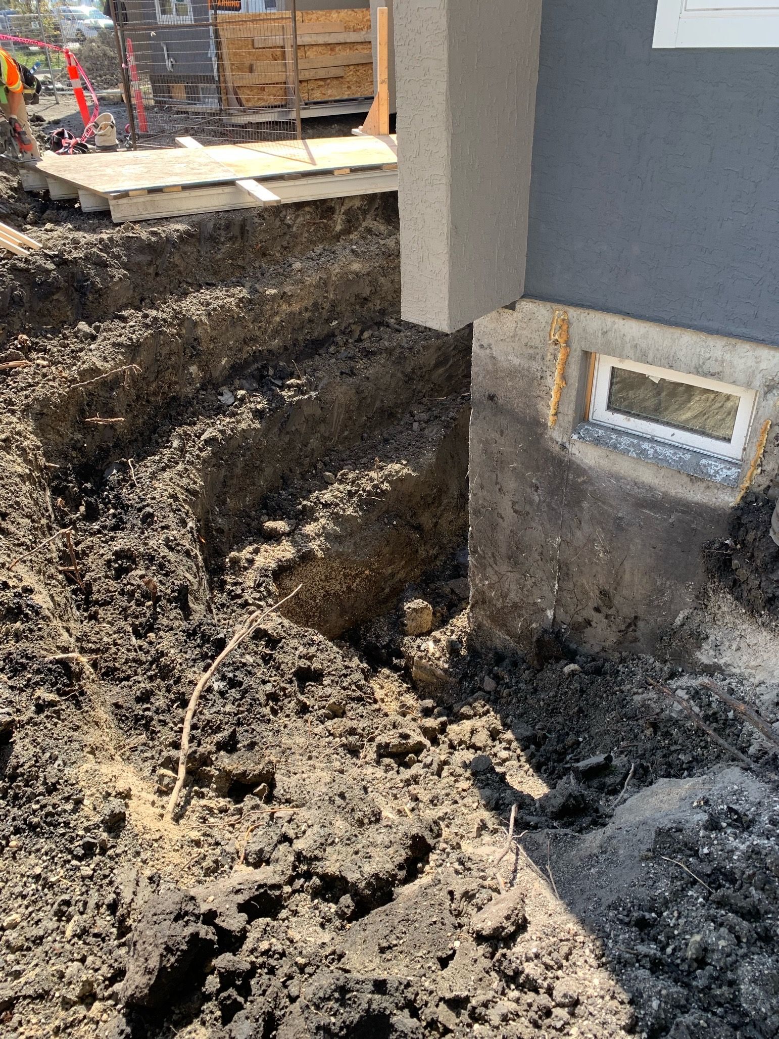Trench dug next to a building's foundation, exposing a window. Construction site.