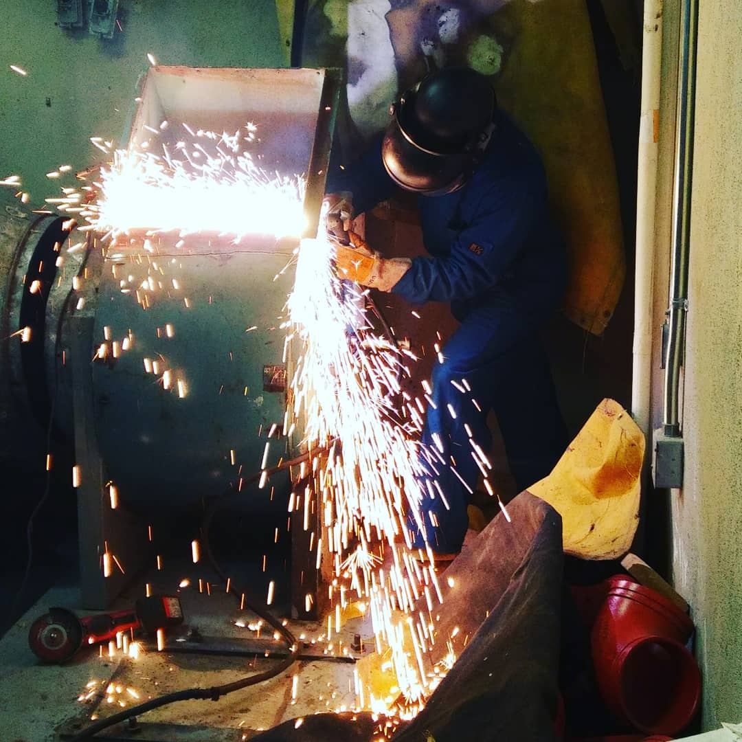 A man wearing a gas mask is welding a piece of metal