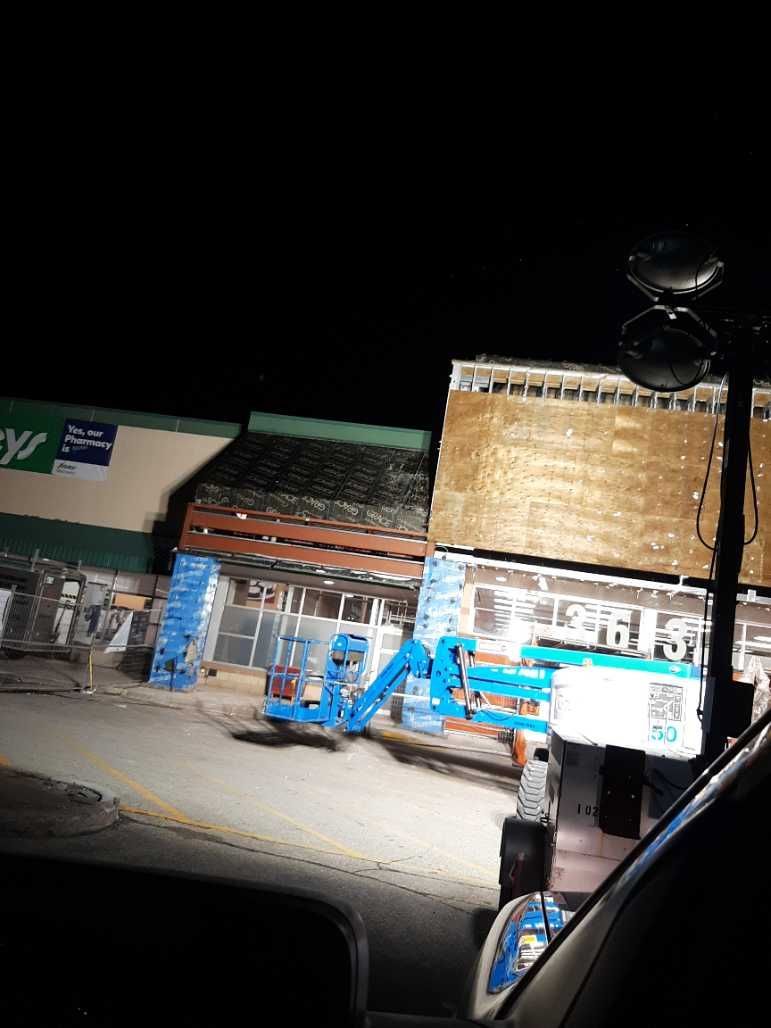 Construction at a store at night, blue lift, and exterior lights on a dark night.