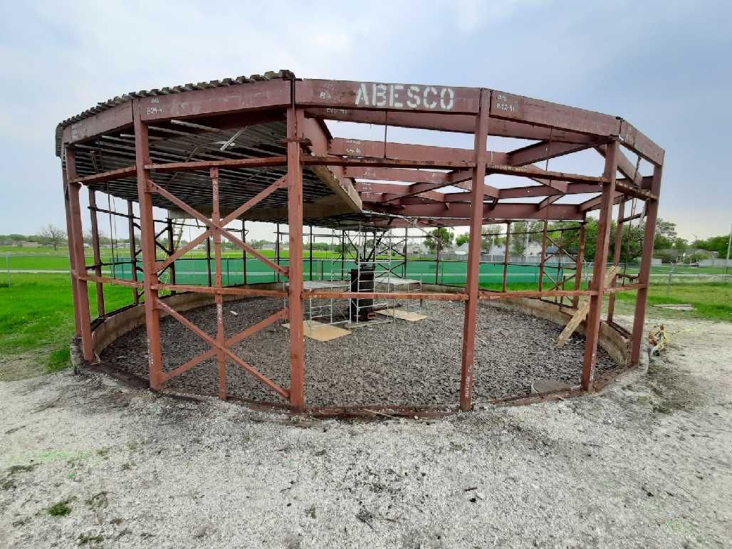 Brown, circular metal structure with ABESCO on top, gravel base, grassy background.