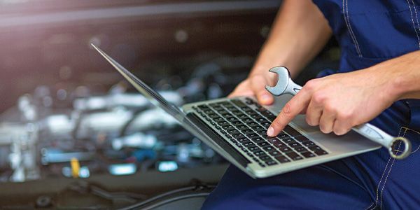 A mechanic is using a laptop computer while holding a wrench.