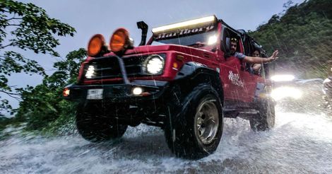 A red jeep is driving through a puddle of water.