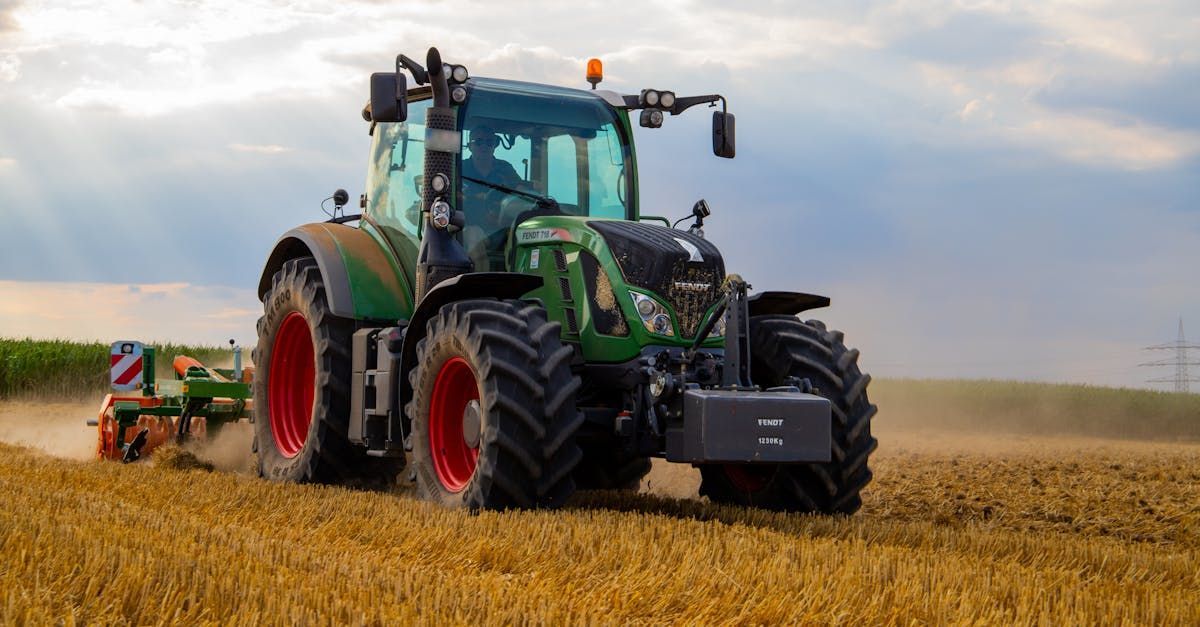 A green tractor with red tires is plowing a field