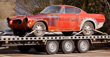A red car is sitting on top of a tow truck.