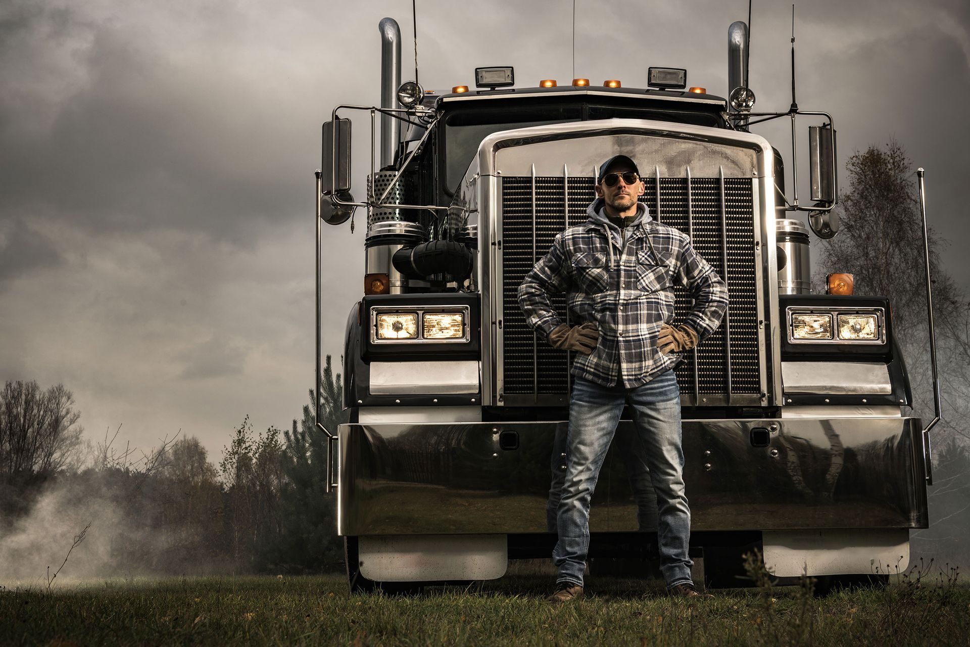 A man in a plaid shirt stands in front of a semi truck