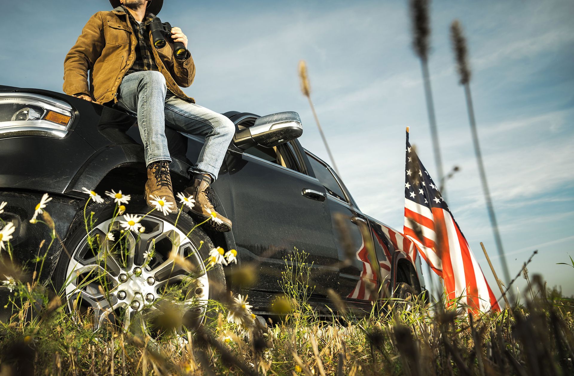 A man in a cowboy hat sits on the hood of a car
