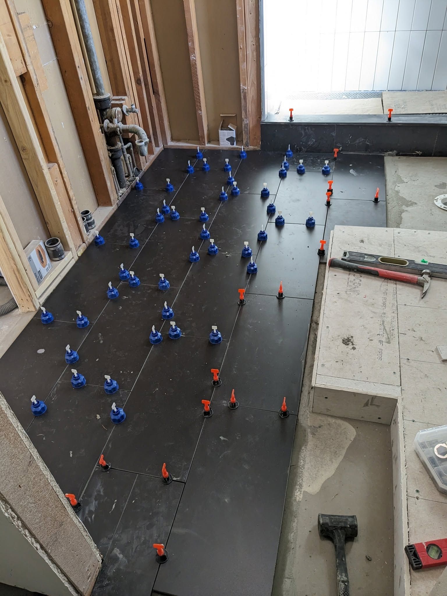 Construction site with many blue and orange markers laid out on a dark floor near unfinished walls.