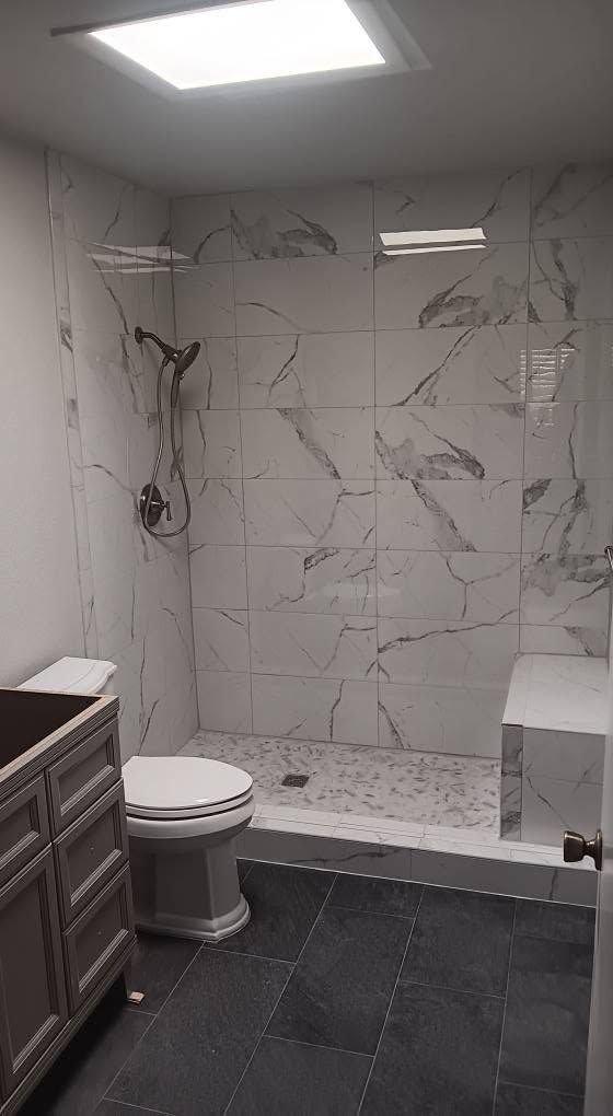 Modern bathroom with marble shower wall, toilet, dark tile floor, and vanity cabinet