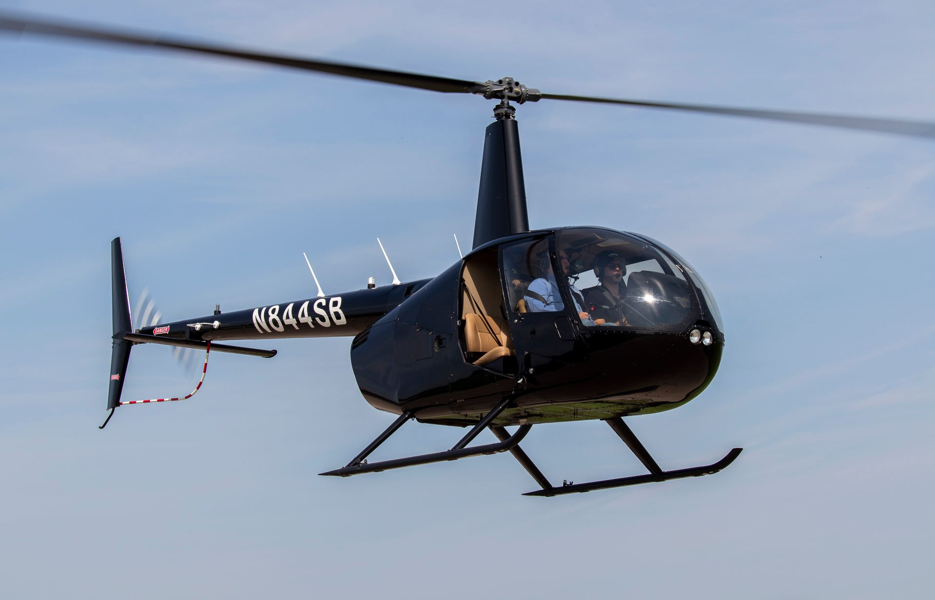 Black helicopter in flight against a blue sky, with white registration number and landing skids.