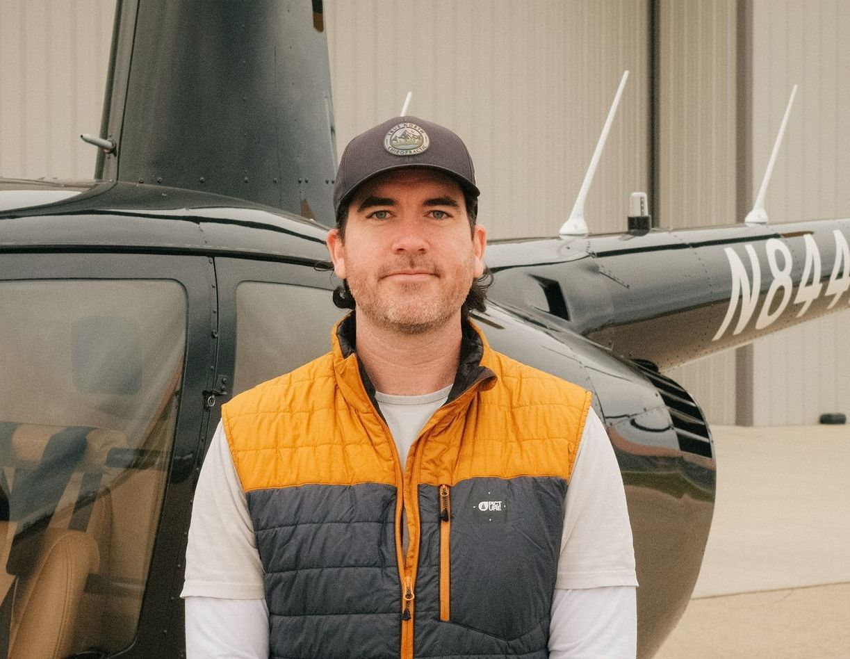 A man is standing in front of a black helicopter in a hangar.