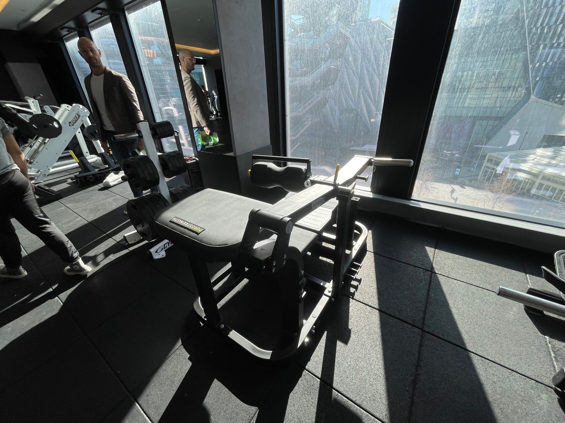 Gym installation in progress with trainers setting up equipment near large windows.