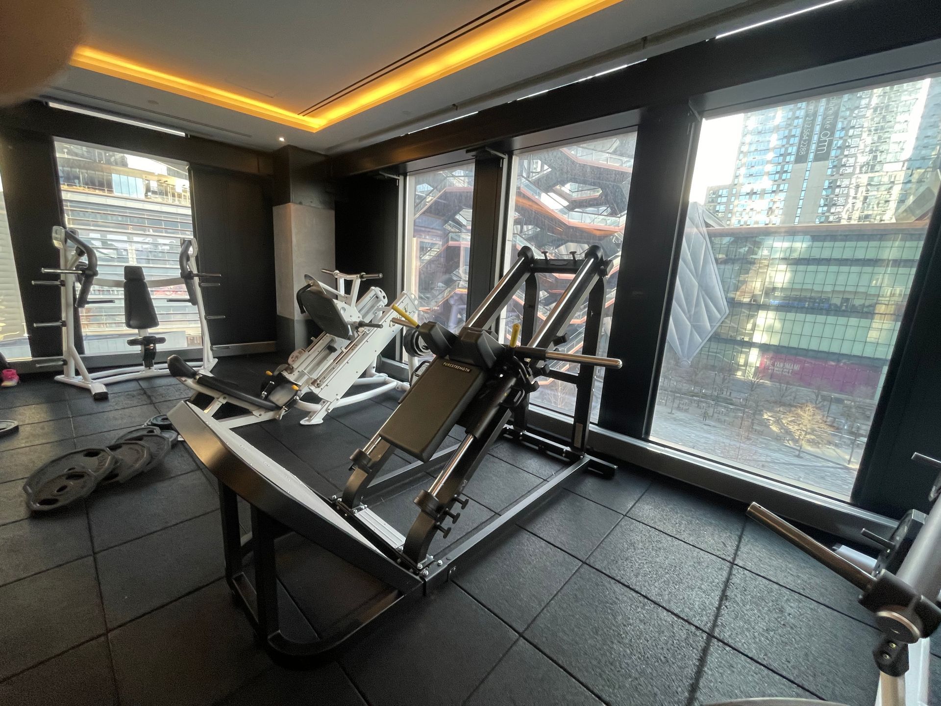 Leg press machine installed in a modern high-rise gym with city view.