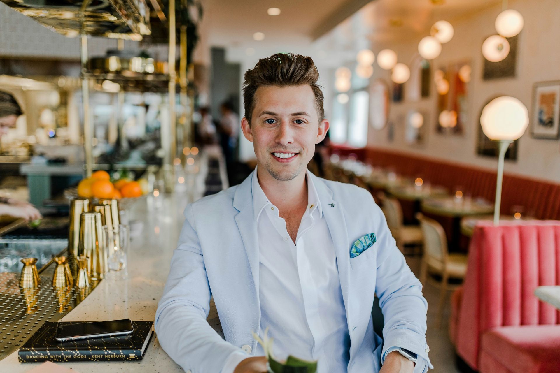 Man in light blue blazer smiles at the bar of a restaurant.