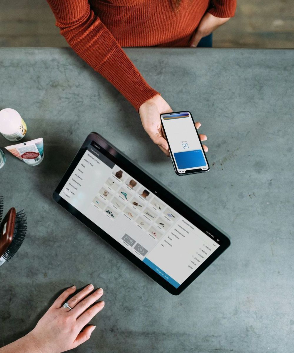 Person using smartphone to pay at a point-of-sale tablet on a gray counter.