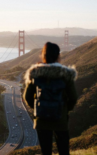 Person with backpack overlooking the Golden Gate Bridge and highway at sunset.