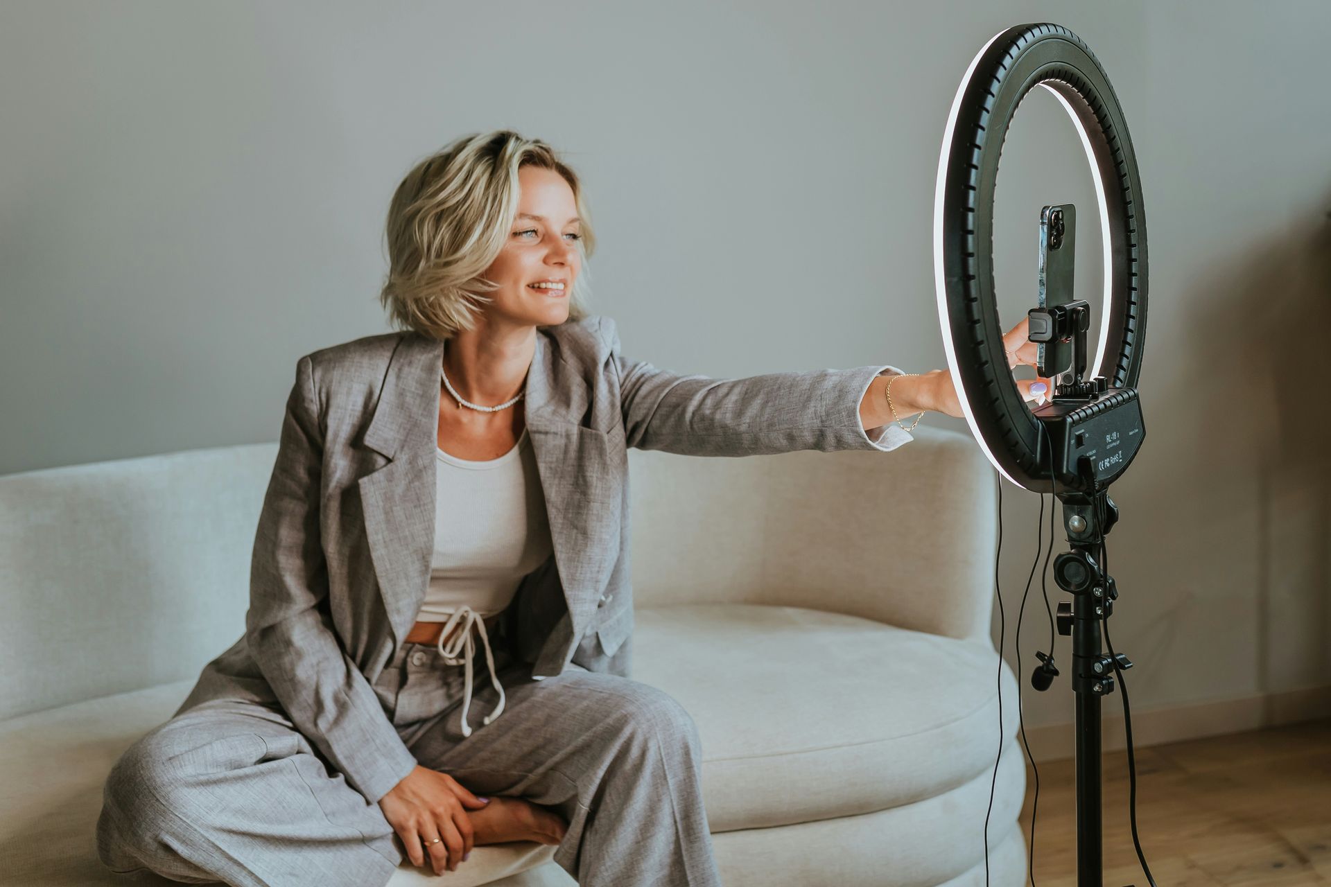 Woman adjusting ring light while sitting on a couch.