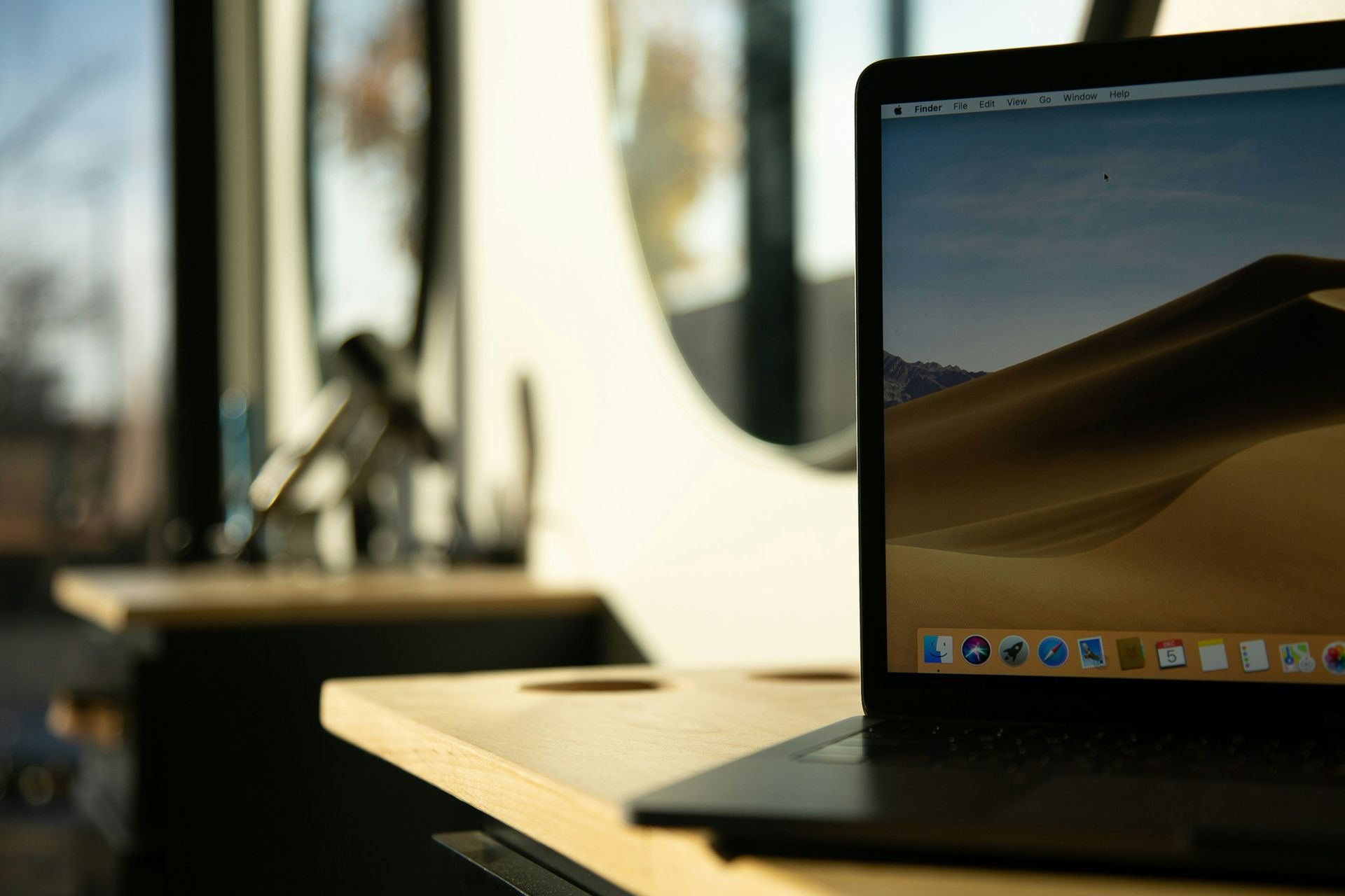 Laptop on a wooden desk with a desert wallpaper. A window and interior are blurred in the background.
