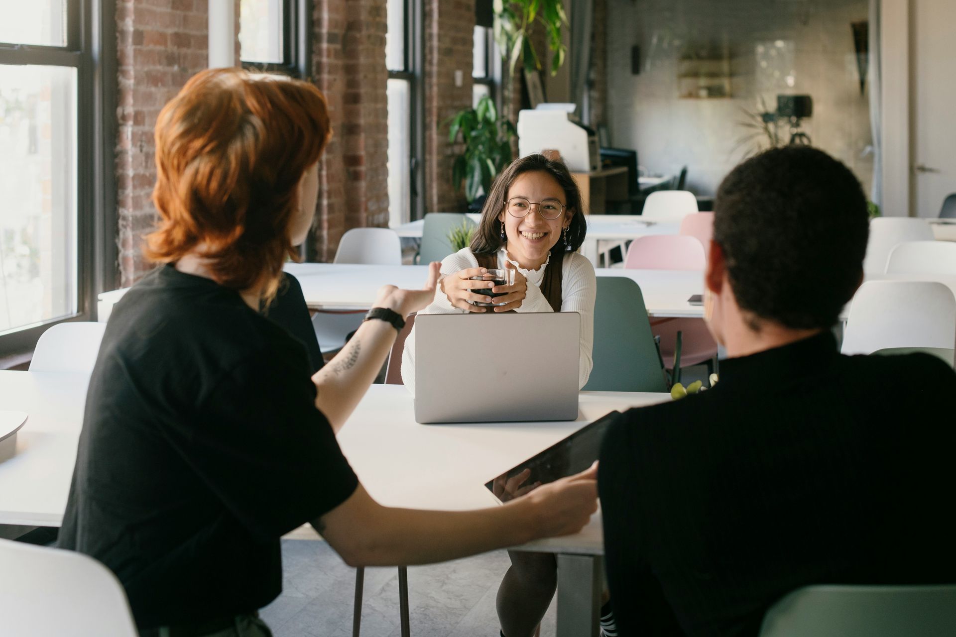 Three people in a modern office, one using a laptop, interacting around a table.