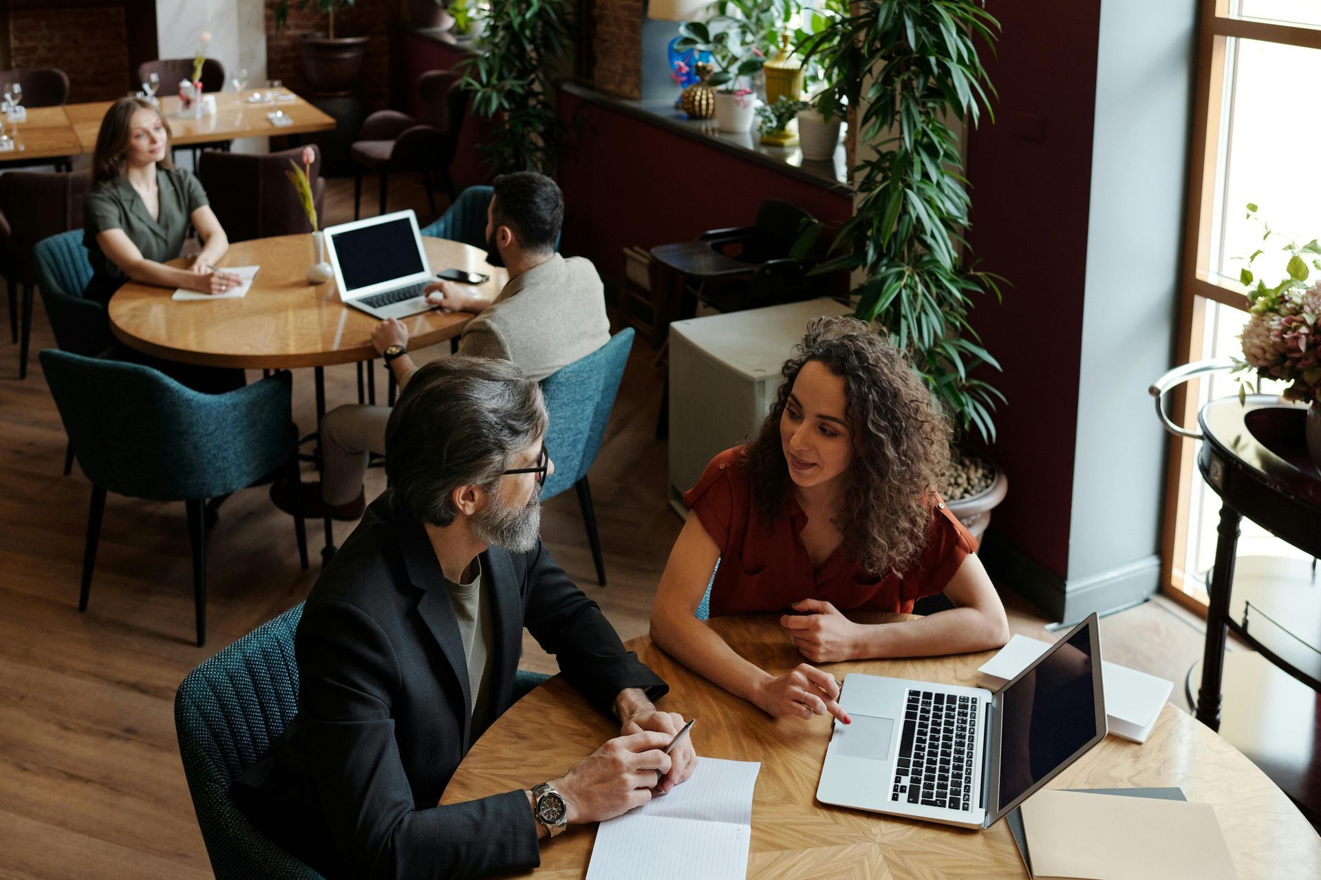 People at round tables in a cafe, some working on laptops and interacting.
