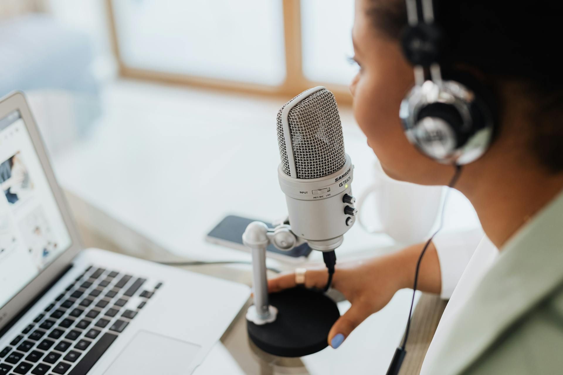 Person wearing headphones speaking into a microphone near a laptop.