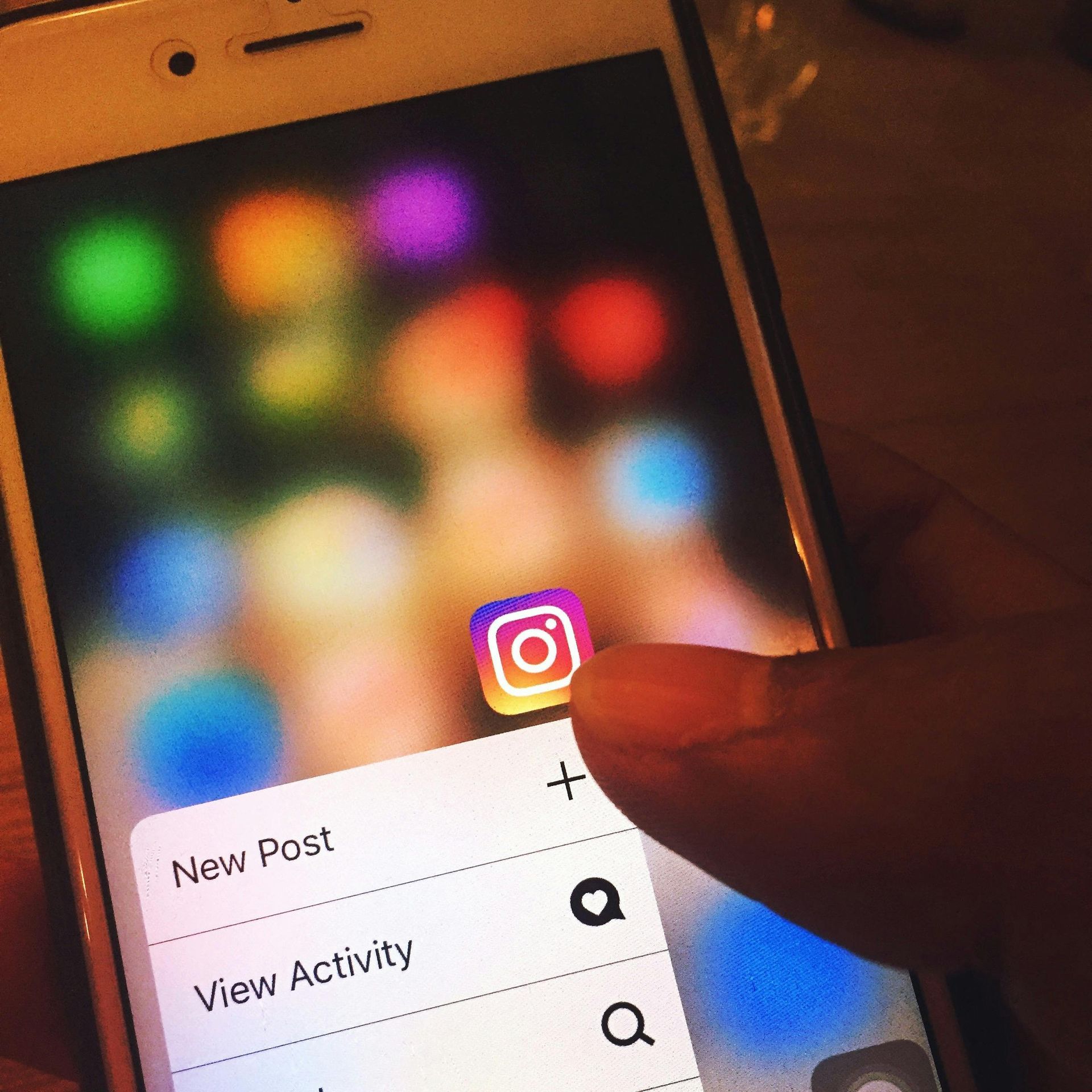 Finger touching an Instagram app icon on a phone screen, with options for new post and activity.
