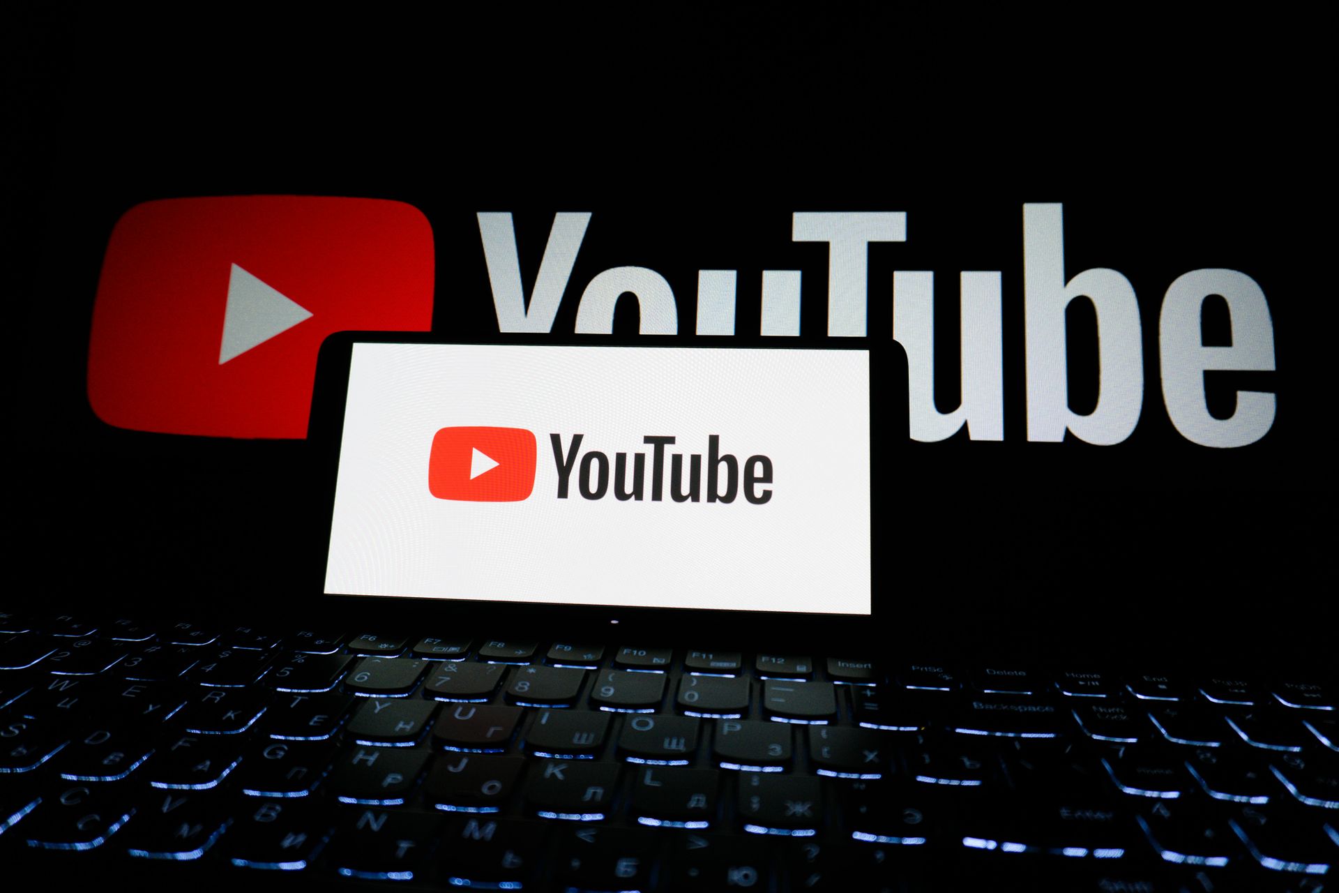 YouTube logo with a red play button, displayed on a laptop screen and in the background.