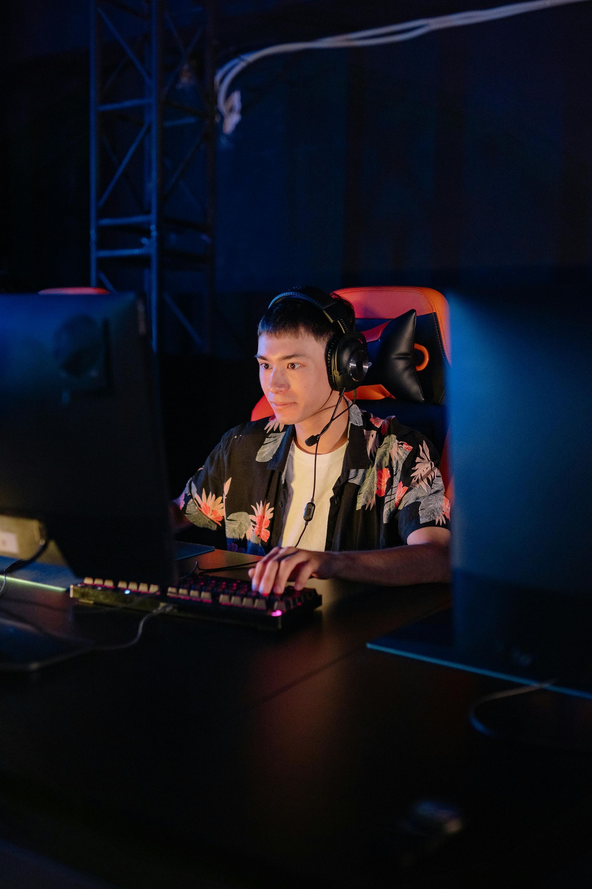 Person wearing a headset, intently playing a game at a computer with a colorful keyboard, in a dimly lit setting.