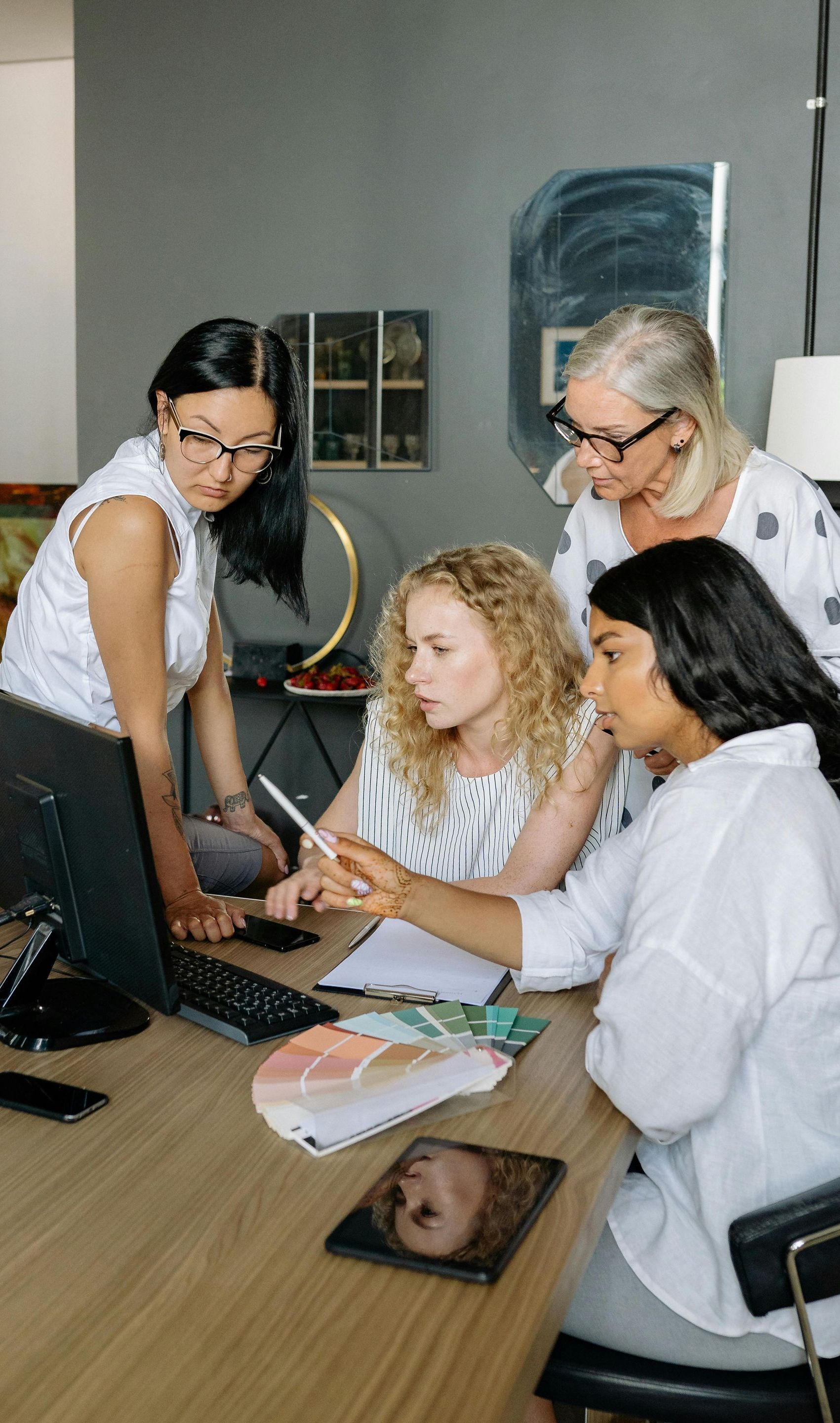 Four people gather around a table, collaborating on a design project, pointing at a tablet and palette.