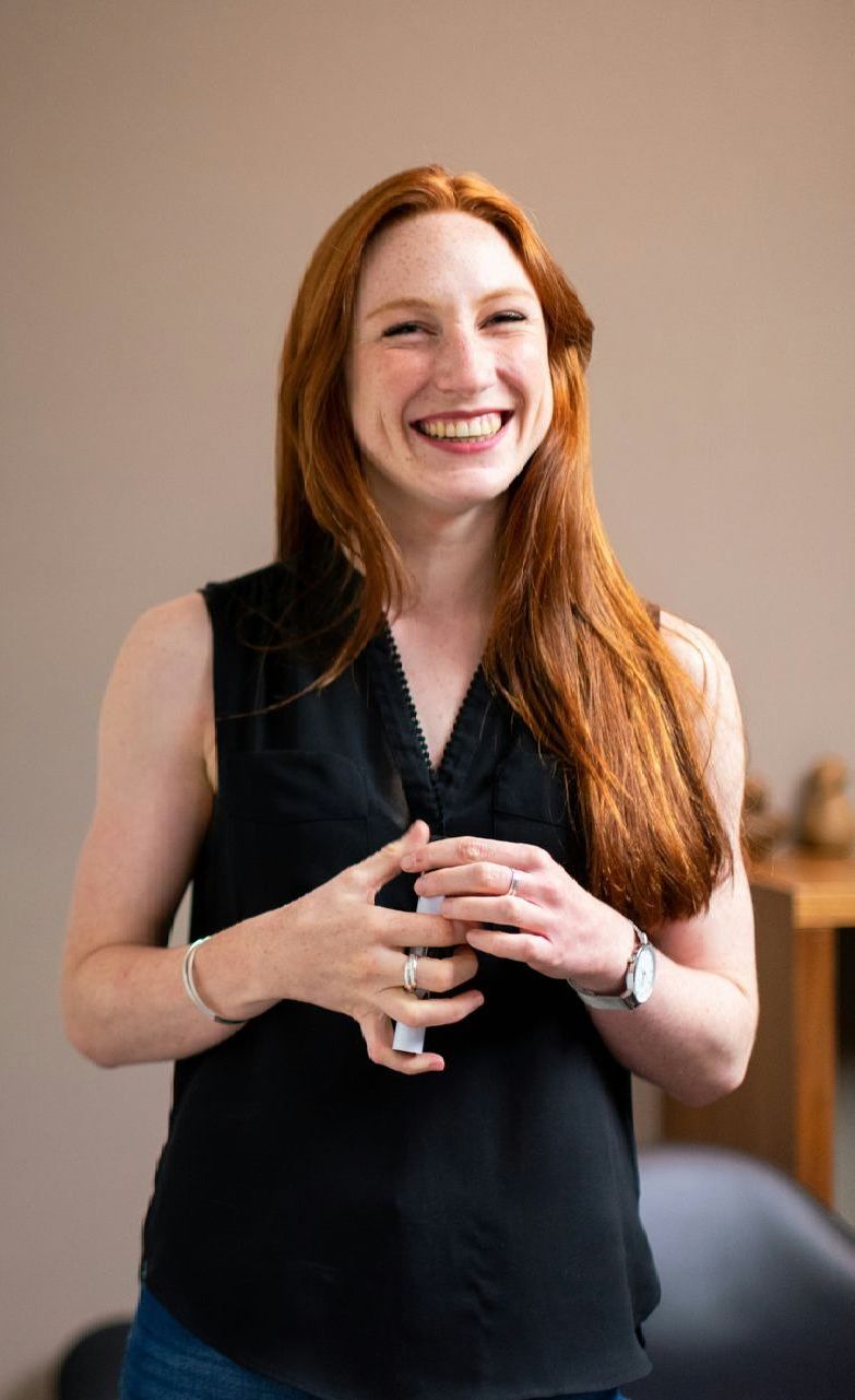 Woman with red hair smiling, wearing a black sleeveless top, indoors.