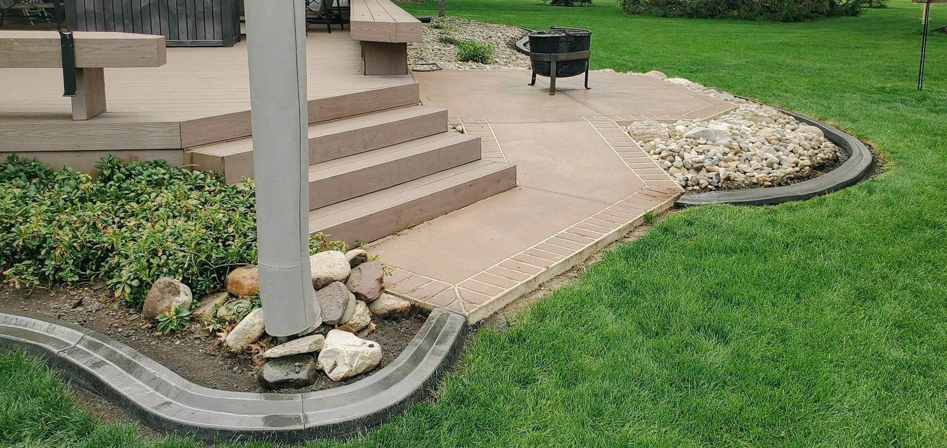 A concrete patio with a fire pit, steps, and a lush green lawn.