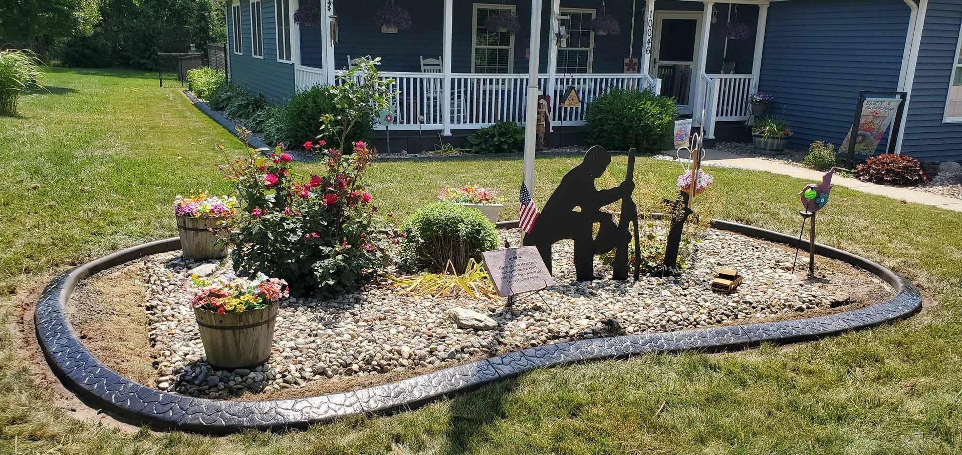 A landscaped garden bed with a metal soldier statue in front of a house.