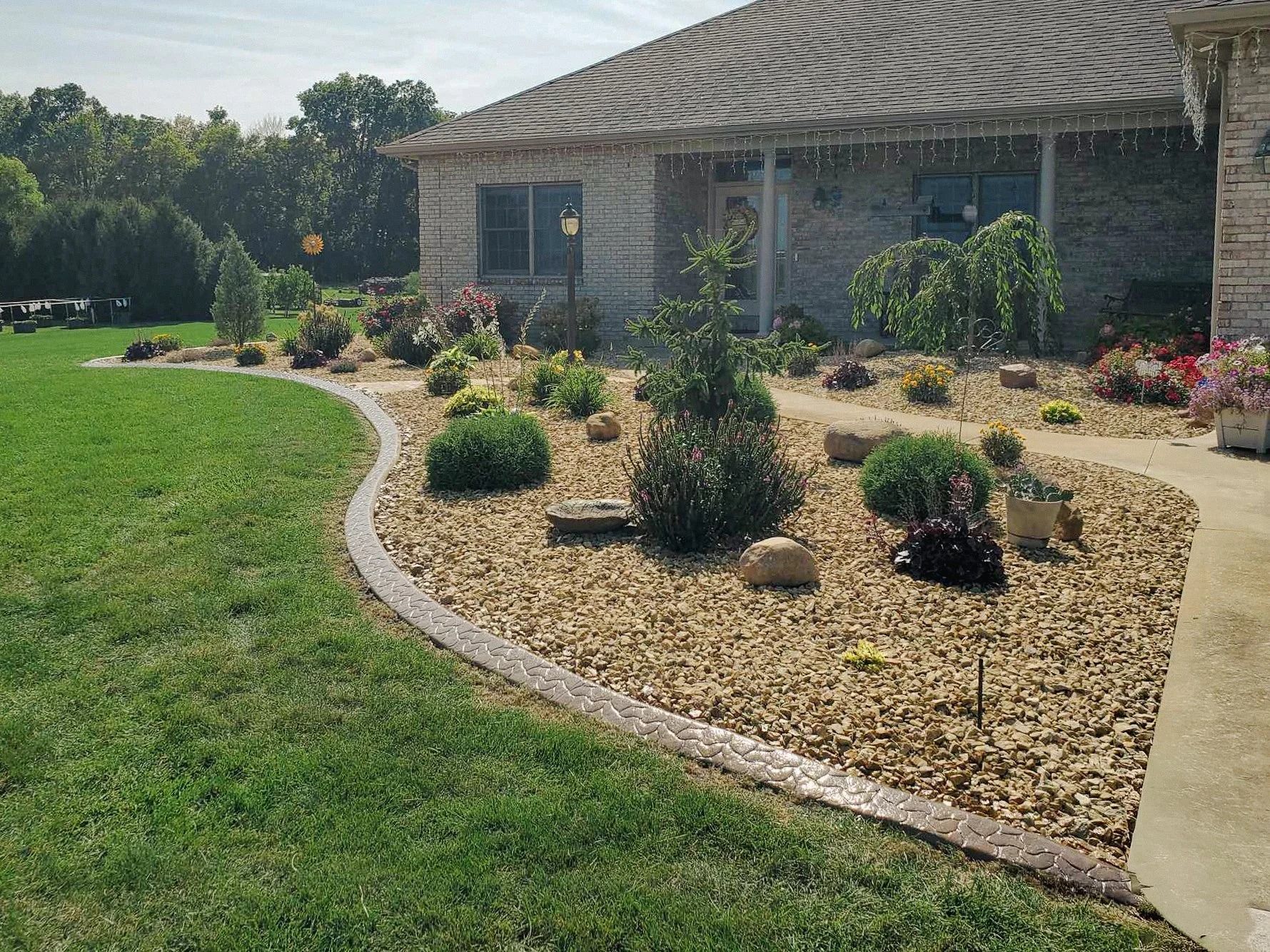 House exterior with rock landscaping bed, lush lawn, and brown concrete edging.